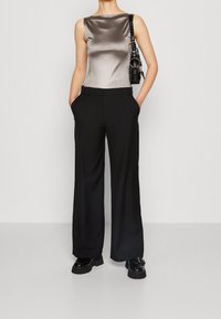 Metaliczna szara bluzka bez rękawów w połączeniu z czarnymi szerokimi spodniami, posiadającymi gładką fakturę oraz elegancką torebkę z srebrnymi akcentami.
