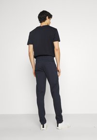 Pantalon navy slim fit, avec des poches arrière et des détails de taille subtils, associé à un t-shirt noir à manches courtes et des baskets blanches.