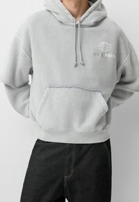 Felpa con cappuccio grigia chiara, dotata di tasca frontale, dettagli a taglio grezzo e ricamo del logo. Composizione in misto cotone con vestibilità comoda.
