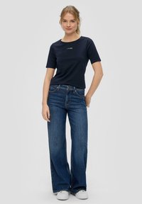 Navyblauwe katoenen t-shirt met korte mouwen en ronde hals, gecombineerd met wijde donkerblauwe jeans en witte sneakers. Eenvoudig logootje op het shirt.