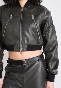 Skórzana czarna kurtka typu bomber ze srebrnymi zamkami, o fakturowanej powierzchni, z prążkowanym kołnierzem i mankietami, w zestawieniu z wysokim stanem skórzaną spódnicą.