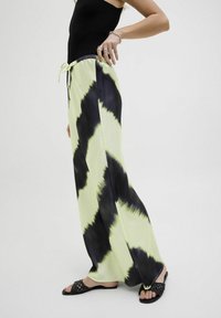 Lichtgroene en zwarte tie-dye wijde pijpenbroeken met een elastische tailleband en trekkoord, met een gladde, vloeiende stofstructuur.