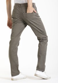Pantalon slim-fit vert olive en coton léger, comprenant deux poches arrière et un design à l'avant plat. Assorti à des baskets blanches.