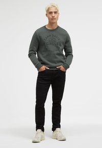 Gray sweatshirt with embossed print, black jeans, and neutral sneakers. The sweatshirt has ribbed cuffs and a round neckline.
