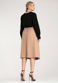 Czarna bluzka z długim rękawem z tylnym karczkiem, zestawiona z beżową spódnicą do kolan z elastycznym pasem. Czarne sandały na wysokim obcasie z ramiączkami.