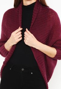Bordeauxroter Strickcardigan mit offenem Vorderteil, strukturiertem Muster und gerippten Kanten, mit lockerem Sitz und langen Ärmeln.