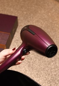 Hårtork i metallisk vinröd färg med slät yta, utrustad med en sidoknapp och ett texturerat luftutsläppsgaller. Kartong delvis synlig.