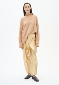 Light beige turtleneck sweater, gold pleated trousers, and black slip-on shoes. Simple shapes and soft textures with a minimalist design.