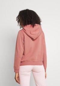 Felpa con cappuccio in rosa polveroso, con una vestibilità rilassata, texture morbida, polsini e orlo a costine. Presenta una tasca a marsupio sul davanti.