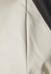 Deux sections de tissu : l'une de couleur crème et texturée, l'autre noire et lisse. La couture traverse verticalement le centre de l'image.