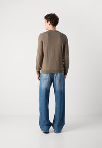 Brun strikkegenser med ribbestrikkede mansjetter og hem, kombinert med løse blå jeans med falmede detaljer og baklommer. Utsikt fra baksiden.
