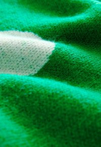 Makro snimka zelenog i bijelog pletenog tkanja s mekanom, paperjastom teksturom i vidljivim vlaknima prediva.