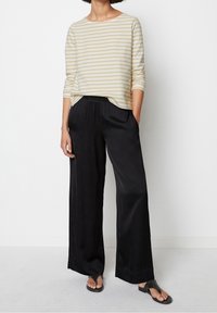 Beige overhemd met lange mouwen en horizontale strepen, gecombineerd met losse zwarte satijnen broeken en zwarte flip-flops, wat zorgt voor een ontspannen outfit.