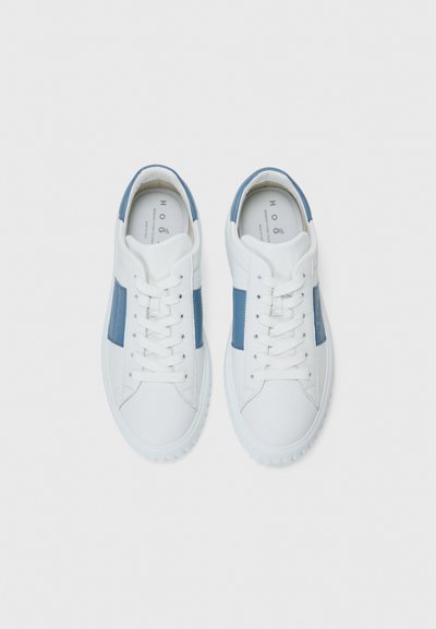 White sneakers with blue leather accents, perforated side panels, and white laces. Soft texture with a rounded toe and flat rubber sole.