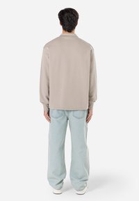 Lys beige sweatshirt med en afslappet pasform, lange ærmer og ribbede manchetter, parret med løse lyseblå jeans og hvide sneakers.