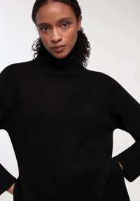 Czarny sweter z golfem wykonany z dzianiny, z długimi rękawami i luźnym krojem. Subtelna tekstura na całej powierzchni materiału.