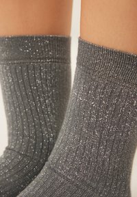 Calzini grigi a coste con una texture scintillante, caratterizzati da un design a metà polpaccio e una vestibilità aderente alla caviglia.