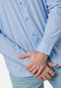 Camisa de botones de color azul claro con mangas largas, que presenta un patrón sutil y cierre de botones, hecha de una tela suave y ligera.
