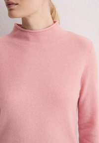 Jasnoróżowy sweter z wysokim kołnierzem, wykonany z miękkiej dzianiny; posiada długie rękawy i gładkie, teksturowane wykończenie.