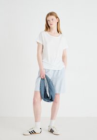 T-shirt blanc à manches courtes associé à une jupe bleu clair, tenant un vêtement en denim. Porté avec des chaussettes blanches et des baskets à rayures noires.