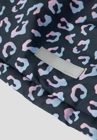 Sort stof med et pastelfarvet leopardmønster. En grå læderlabel med brandnavnet er synlig. Glat tekstur.