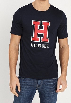 Navy blue cotton t-shirt featuring a large red "H" logo and "HILFIGER" text in white below. Short sleeves and crew neckline.