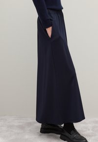 Marineblauwe maxi rok van een gladde, lichte stof, met een elastische tailleband, zijzakken en een rechte snit, gecombineerd met zwarte schoenen.