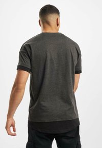 Dunkelgraues T-Shirt mit kurzen Ärmeln, das über einen runden Halsausschnitt und einen kontrastierenden schwarzen Saum verfügt. Der Stoff wirkt glatt mit einer subtilen Textur.