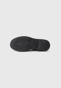 Suela de zapato negra con goma texturizada, surcos de tracción y acentos de patrón circular para un mejor agarre y durabilidad.