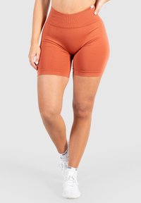 Roestkleurige fietsbroek met een hoge, elastische taille. Gladde textuur, aansluitend ontwerp en lengte tot halverwege de dij. Gecombineerd met witte sportschoenen.