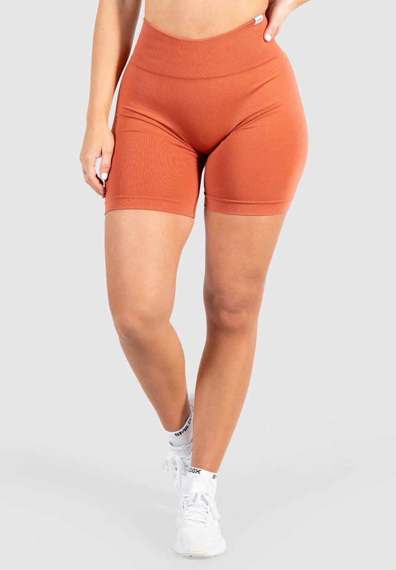Roestkleurige fietsbroek met een hoge, elastische taille. Gladde textuur, aansluitend ontwerp en lengte tot halverwege de dij. Gecombineerd met witte sportschoenen.