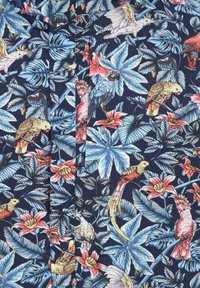 Tissu marine avec un imprimé tropical comportant de grandes feuilles bleues, divers perroquets colorés et des fleurs roses, mettant en valeur des détails complexes.