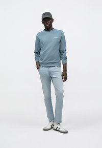 Ανοιχτό μπλε φούτερ με στρογγυλή λαιμόκοψη, ανοιχτό μπλε τζιν, γκρι και λευκά αθλητικά παπούτσια με μαύρες ρίγες και γκρι καπέλο. Καθημερινό ντύσιμο με άνετη εφαρμογή.