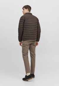 Brun pufferjacka med quiltat mönster, ståkrage och dragkedjestängning. Kombinerad med beige byxor och svarta mockaskor.