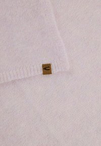Tissu tricoté rose clair avec une texture douce, présentant une petite étiquette marron cousue sur le bord. Le bord a un design côtelé.