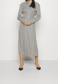Sukienka w czarno-białe wzory w geometryczny kształt, z długimi rękawami, zapięciem na guziki i średniej długości krojem; zestawiona z czarnymi balerinami.