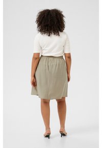 Vue arrière d'une personne portant un top blanc ajusté et une jupe légère olive longueur genoux avec une taille élastique, associée à des sandales.