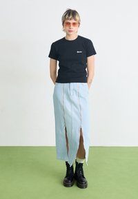 Schwarzes Baumwoll-T-Shirt mit besticktem Logo, kombiniert mit einem hellblauen Jeans-Maxikleid mit zwei Vorderreißverschlüssen und Schlitzen bis zum Oberschenkel. Schwarze Stiefel.