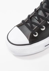 Svart sneakers laget av lær med en hvit gummitåhette. Har svarte snører og metalliske snørehull, med en teksturert hvit yttersåle.