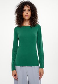 Zielona bluzka z długim rękawem z gładkiego, elastycznego materiału z okrągłym dekoltem, w połączeniu z jasnoszarymi spodniami typu wide-leg. Prosty i dopasowany styl.