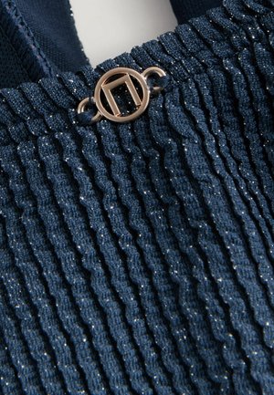 Marineblau gestrickter Stoff mit schimmernder Textur, der vertikale Rippungen aufweist und oben mit einem runden goldenen Hardwareakzent versehen ist.