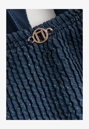 Tumes sinine kudum, millel on särav tekstuur, vertikaalsed sooned ja ülaosas ringikujuline kuldne metallist detail.