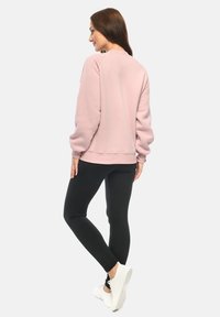 Felpa rosa chiaro con maniche raglan, collo rotondo e orlo a coste, abbinata a leggings neri e sneaker bianche. Texture liscia.