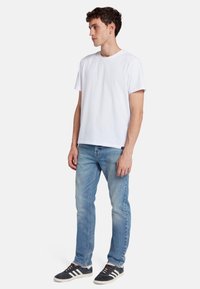 T-shirt bianca in cotone con maniche corte, abbinata a jeans in denim azzurri e sneakers nere con strisce bianche.