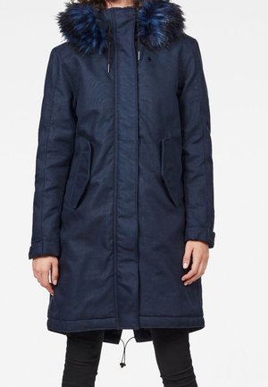 Navy blue parka coat with a faux fur hood, side pockets, and adjustable drawstring at the hem. Made from textured, durable fabric.