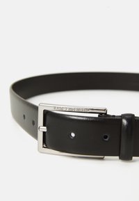 Svart lærbelte med sølvfarget rektangulært spenne gravert med "KARL LAGERFELD" på hvit bakgrunn.