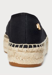 Espadrilles de lien negro con suela de yute, que presentan un pequeño acento de hardware dorado en el talón y un detalle de costura a lo largo del borde.
