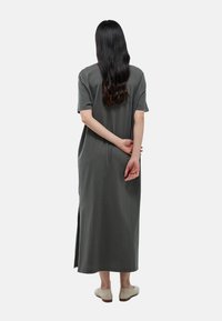 Robe grise, longueur genou, en tissu doux, avec des manches courtes et des fentes sur les côtés. Le modèle porte des chaussures claires, avec les cheveux lâchés.