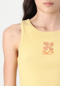Yellow ribbed tank top featuring a floral logo in orange embroidery on the left side near the neckline. Smooth texture with narrow straps.