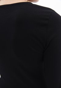 Schwarzes, eng anliegendes Oberteil mit einer glatten, weichen Textur, mit Rundhalsausschnitt und langen Ärmeln, von hinten betrachtet.